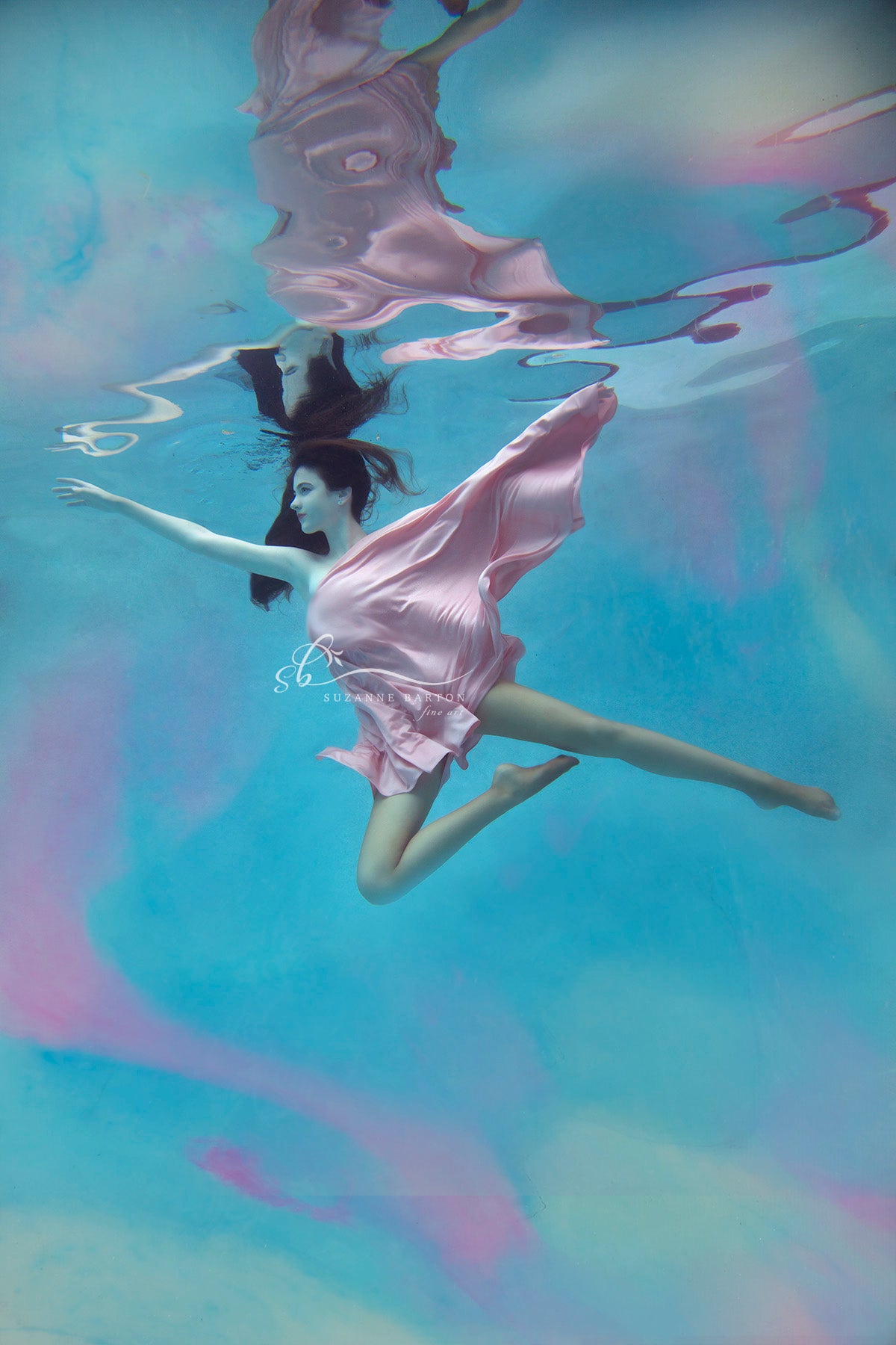 Woman in soft pink gliding through the aqua blue of underwater. She surrounded by swirls of the same soft pink.