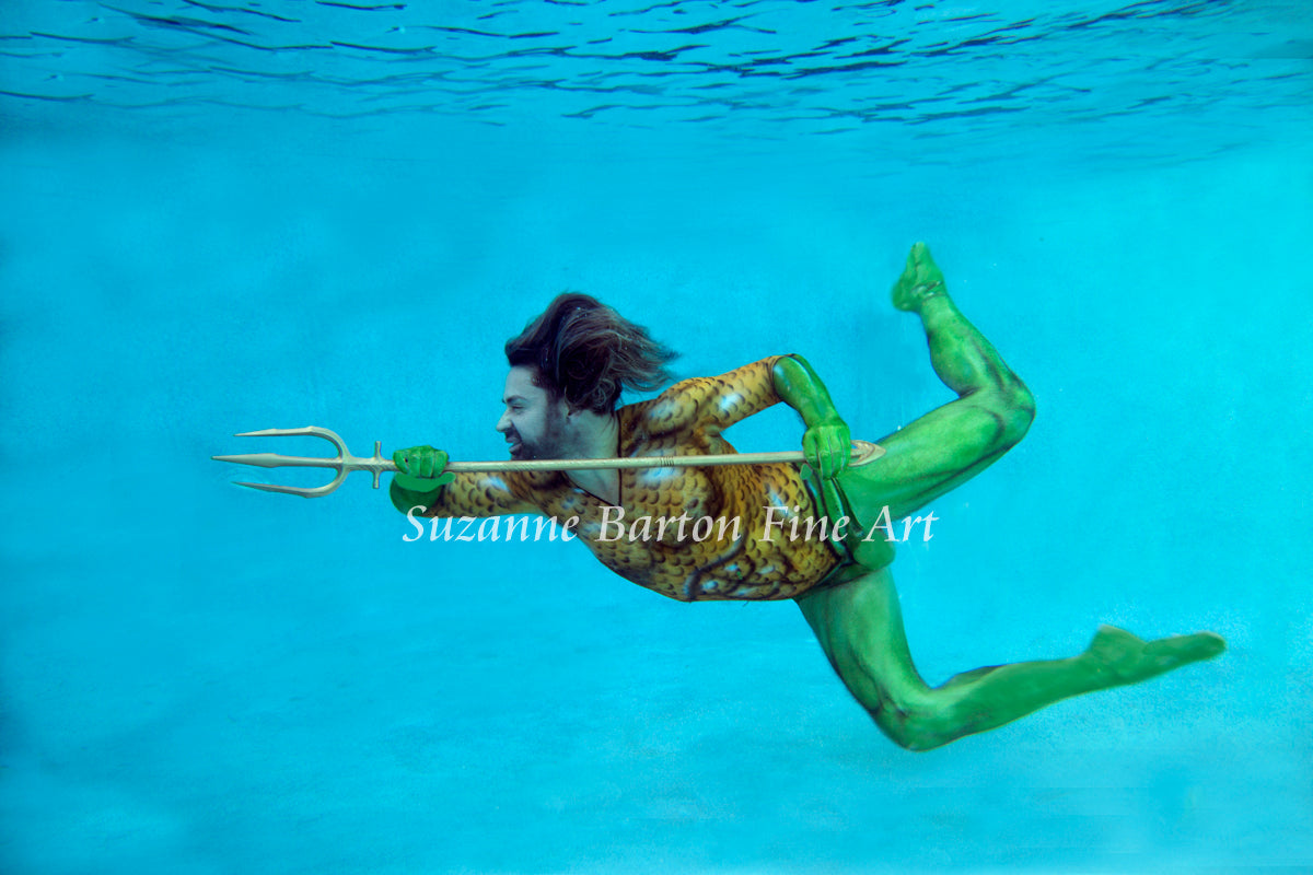 Merman underwater swimming holding golden trident and pointing to something you cannot see.