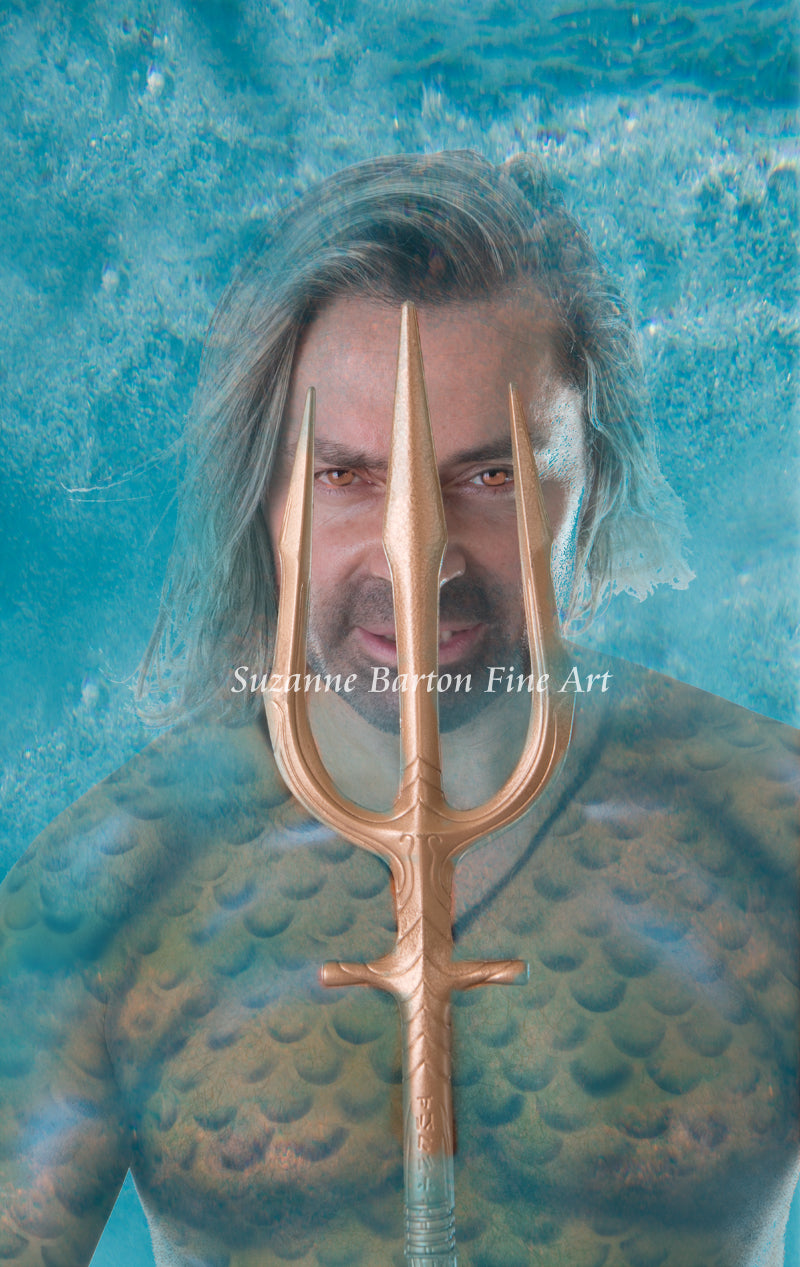 Close-up of a merman's face, chest and his golden trident in an underwater scene.