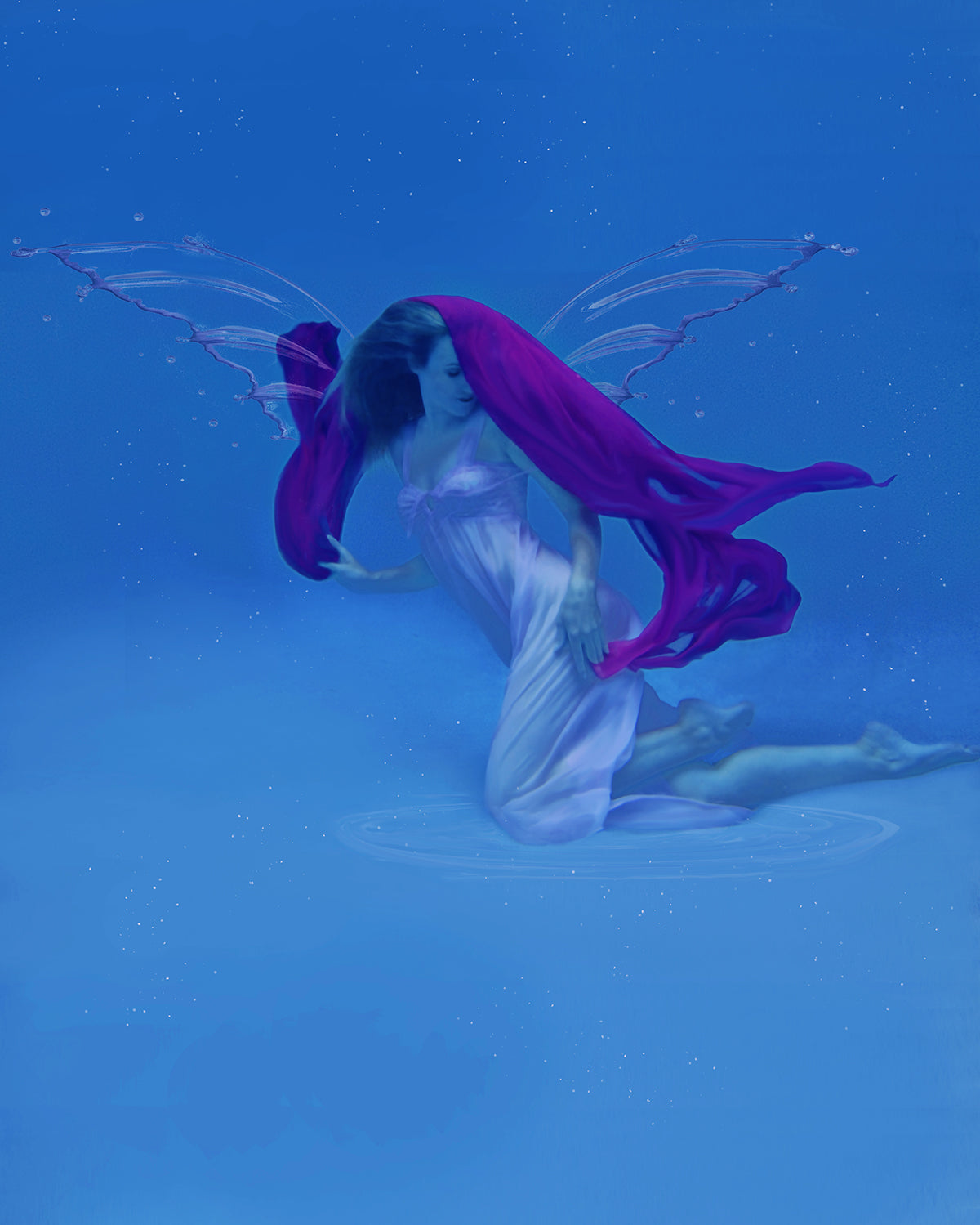 A delicate female figure enveloped in flowing dark pink fabric in an underwater image of blues. The flowy fabric and fluid movement is mesmerizing.