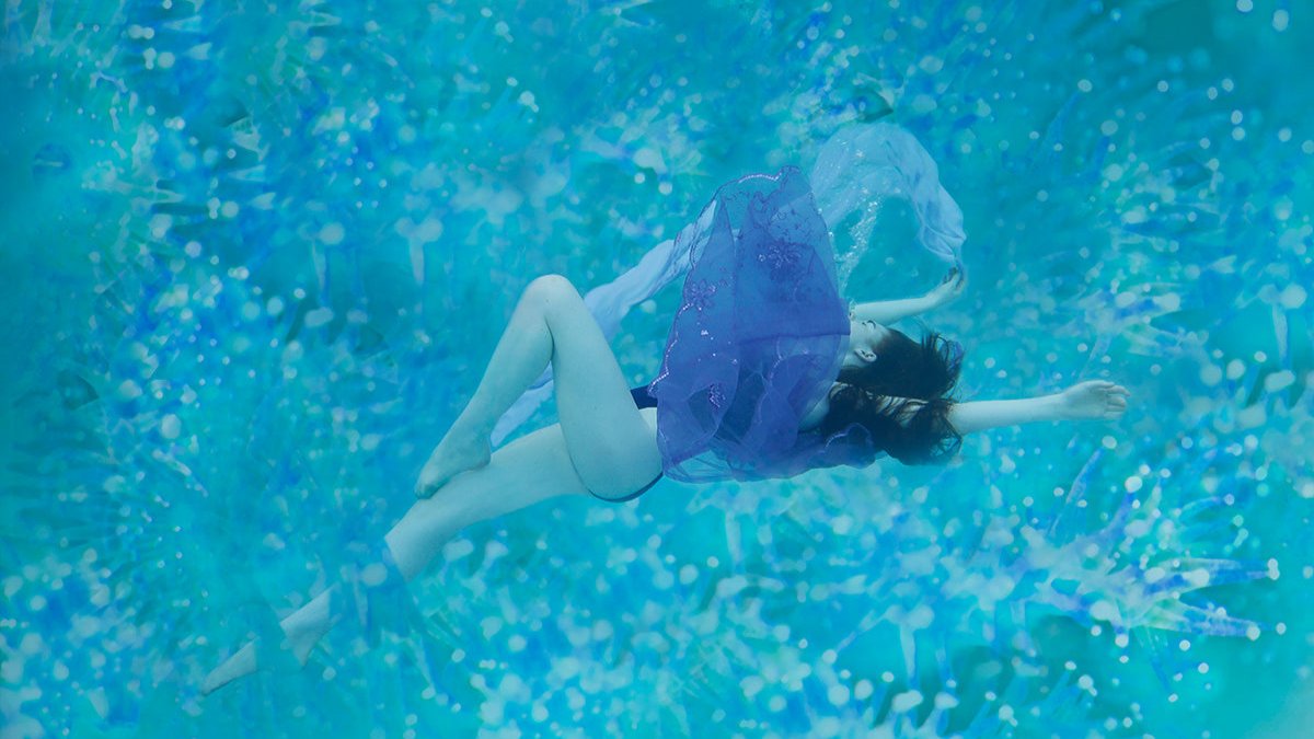 A beautiful woman stretched out underwater with a silk purple scarf flowing artfully in the water.