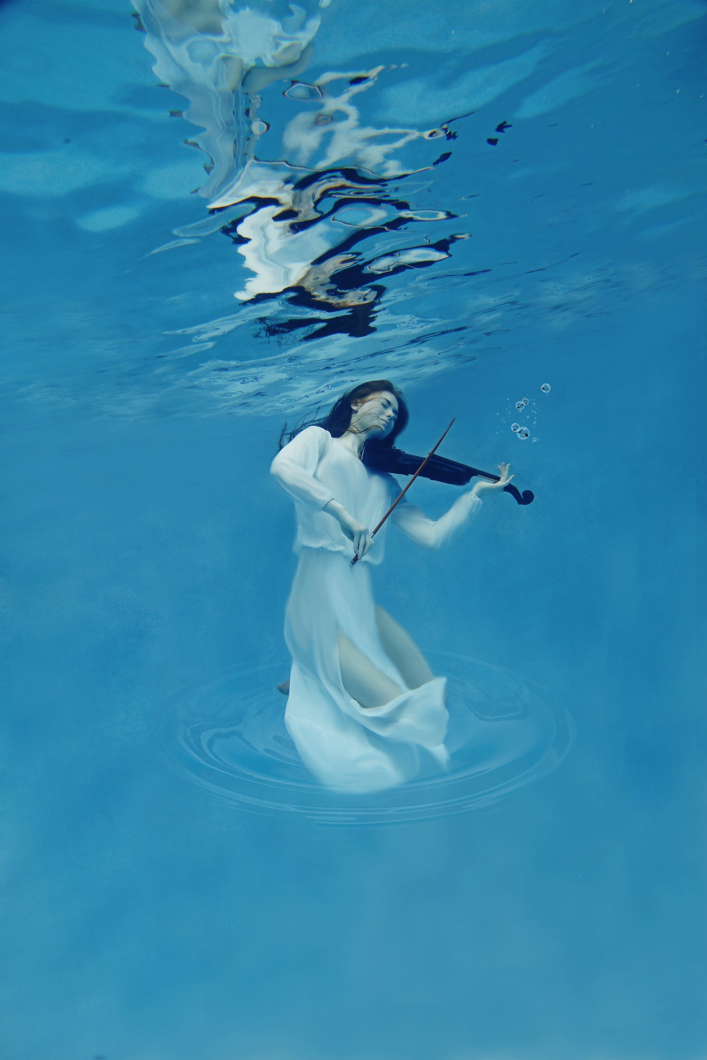 A woman in a flowing white dress  underwater playing the violin portrays a stunning ethereal scene. Angelic Concerto