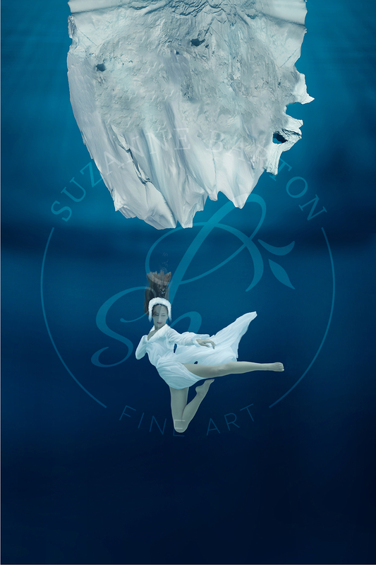 A beautiful young woman underwater below a gorgeous billow of white fabric evoking a swan-like quality.