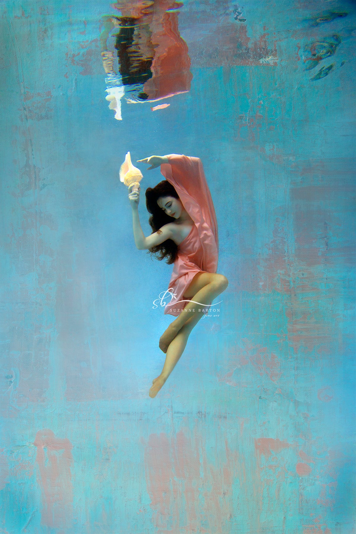 Beautiful woman wrapped in a flowing peach color scarf ertically posed underwater holding a conch shell.