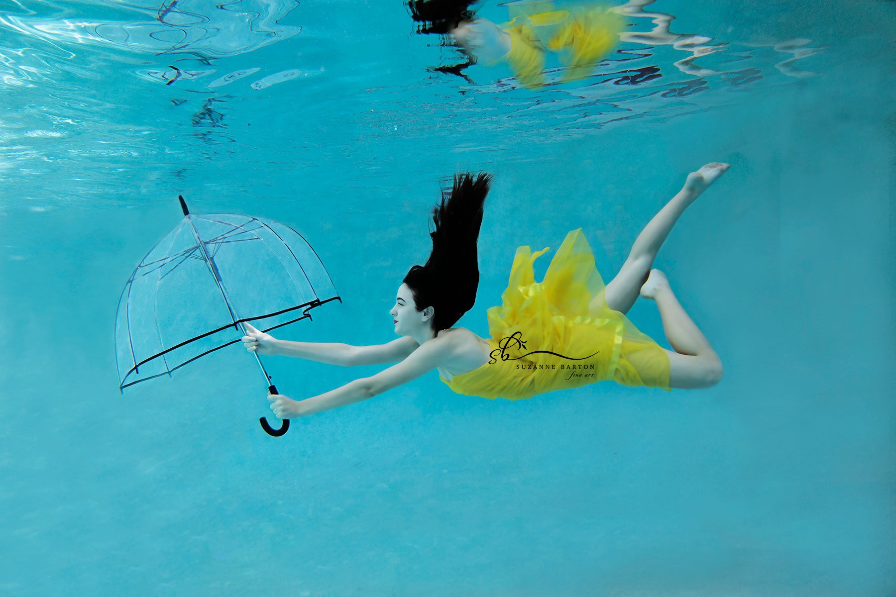 Dark-haired woman wearing a yellow dress and holding an umbrella while floating underwater. 